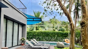 A modern outdoor pool area with lounge chairs, a wooden deck, and a blue awning. - Maribel Villa Phu Quoc 4BR - Private Pool (Phú Quốc)