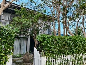 A residential area with a white picket fence, a large tree, and a building with a balcony. - Maribel Villa Phu Quoc 4BR - Private Pool (Phú Quốc)