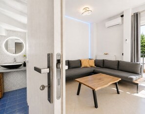 Una sala moderna con un sofá seccional, una mesa de centro y una cocina con pileta y espejo.