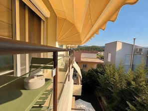 Un balcón con un toldo amarillo, una mesa verde y una maceta de piedra.