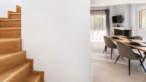 A modern interior with a wooden staircase, a dining area with a long table and chairs, and a fireplace.