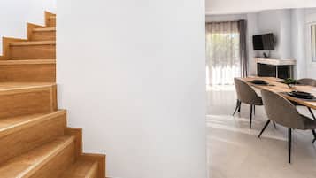 Un interior moderno con una escalera de madera, una zona de comedor con una mesa larga y sillas, y una chimenea.
