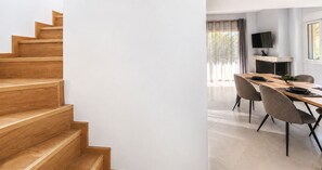 Un interior moderno con una escalera de madera, una zona de comedor con una mesa larga y sillas, y una chimenea.