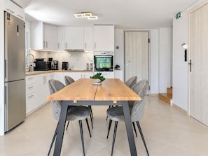 Una cocina moderna con armarios blancos, una mesa de comedor de madera y sillas tapizadas en gris.