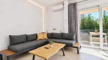 Una sala de estar moderna con un sofá seccional gris, una mesa de centro de madera y un balcón con vista a zonas verdes.
