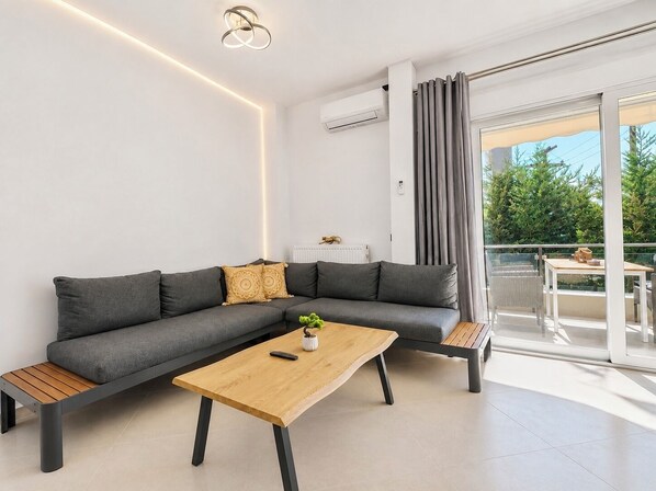 Una sala de estar moderna con un sofá seccional gris, una mesa de centro de madera y un balcón con vista a zonas verdes.