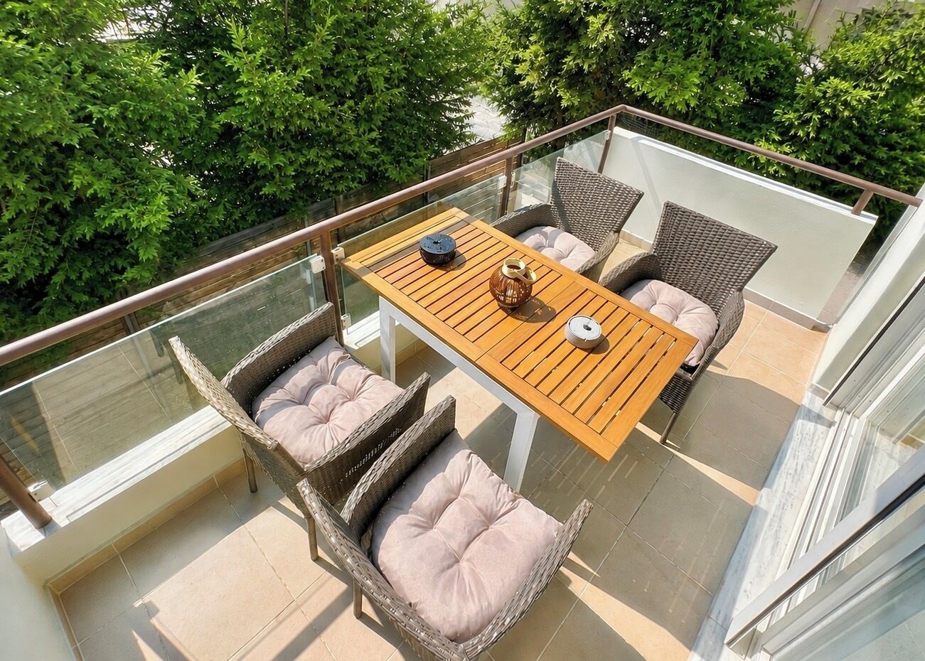 A balcony with wicker furniture, a wooden table, and a glass railing.