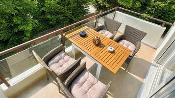 A balcony with wicker furniture, a wooden table, and a glass railing.