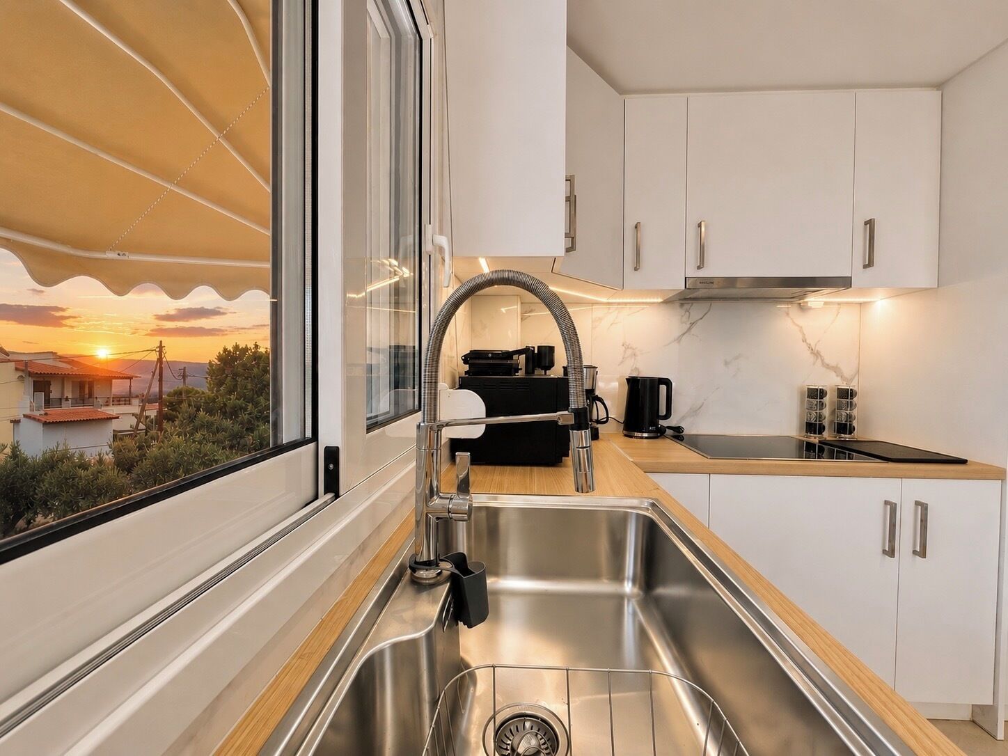 Uma cozinha moderna com uma pia de aço inoxidável, uma máquina de café preta e vista para o pôr do sol pela janela.