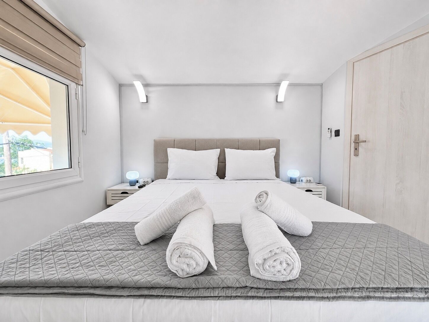 Una camera d'albergo con un letto, due comodini, una finestra e una porta.