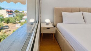 A bedroom with a bed, bedside table, lamp, and a window with a view of the outside.