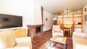 A living room with a fireplace, a television, and a dining area with chairs and a table. - House 2 – Comfortable Vacation Home on Theodor-Storm-Straße (Langeoog)