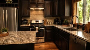 Una cocina con armarios de madera oscura, electrodomésticos de acero inoxidable, encimeras de granito y un ventanal con vistas a árboles.