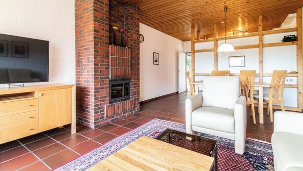 A living room with a brick fireplace, a television, a sofa, and a dining area with wooden furniture. - House 1 on Polderweg – Cozy accommodations with room for 6 guests (Langeoog)