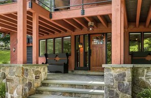 Un bâtiment à deux étages, doté de fondations en pierre, d’une terrasse en bois et d’une grande porte d’entrée en verre.