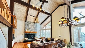 A spacious living area with a fireplace, leather sofa, dining table, and a view of the outdoors. - Luxury 4-bedroom Ski house in Stratton with Shuttle or Walk to Slope Options (Stratton)
