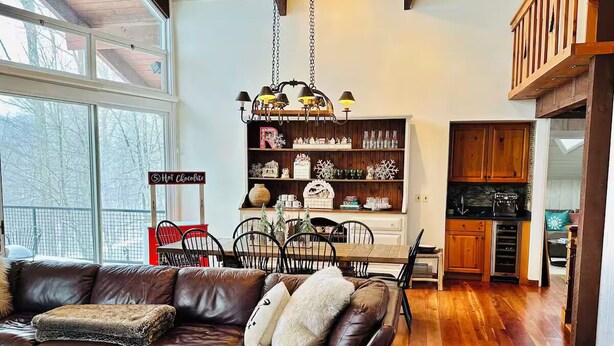 A cozy living room with a leather sofa, a wooden dining table, and a kitchen area with wooden cabinets and a hanging light fixture. - Luxury 4-bedroom Ski house in Stratton with Shuttle or Walk to Slope Options (Stratton)