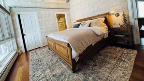 A bedroom with a wooden bed, a nightstand, a lamp, and a window. - Luxury 4-bedroom Ski house in Stratton with Shuttle or Walk to Slope Options (Stratton)