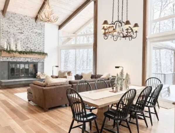 Un salon spacieux avec une cheminée, un coin repas avec une table et des chaises, et de grandes fenêtres.