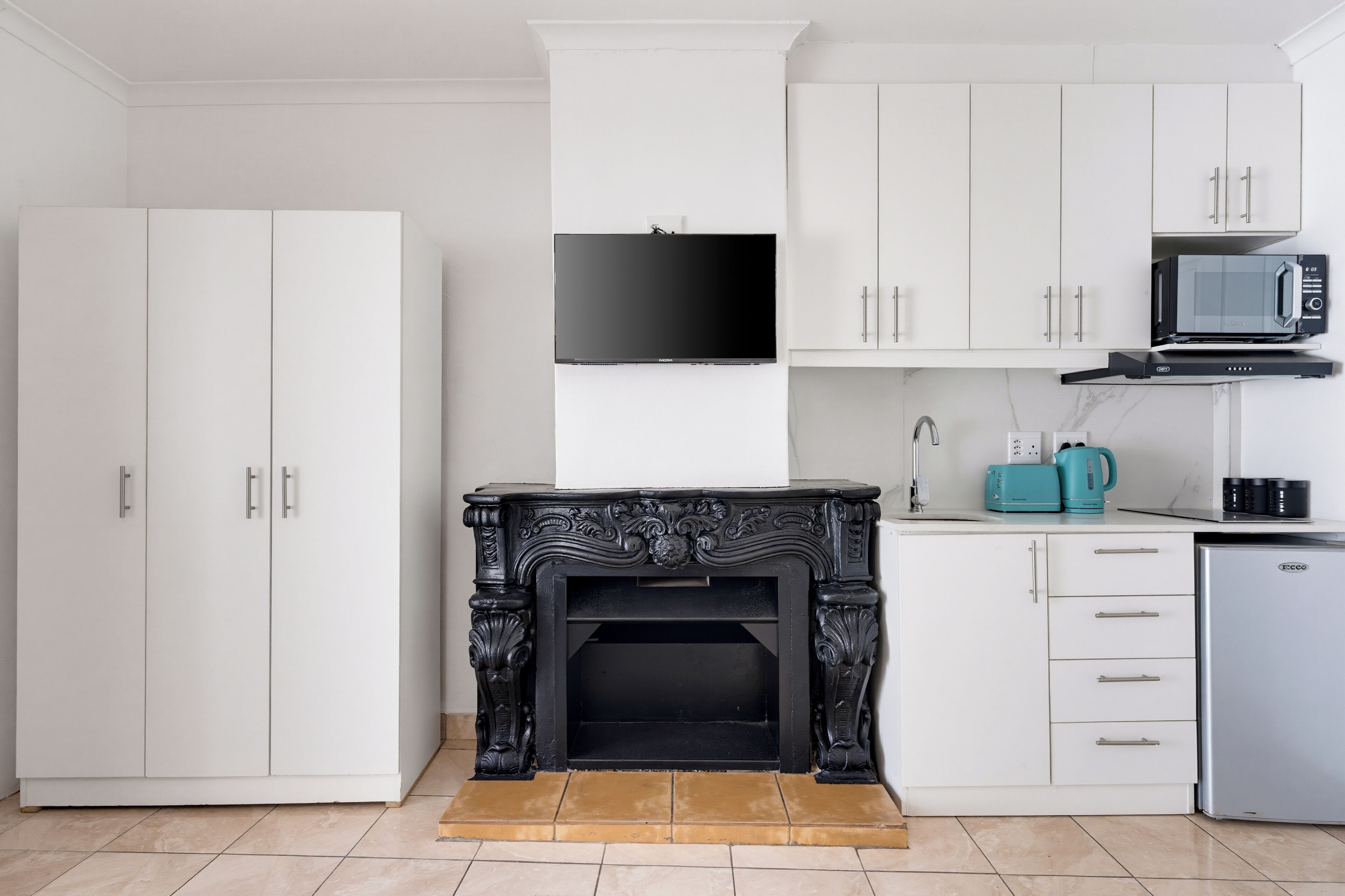 Een moderne keuken met witte kasten, een zwarte open haard, een magnetron en een koffiezetapparaat.
