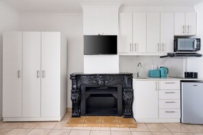 A modern kitchen with white cabinetry, a black fireplace, a microwave, and a coffee maker. - Lion's View Studio Retreat (Cape Town)