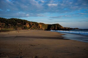 A beach with a rocky outcrop, clear skies, and thatched-roof buildings.