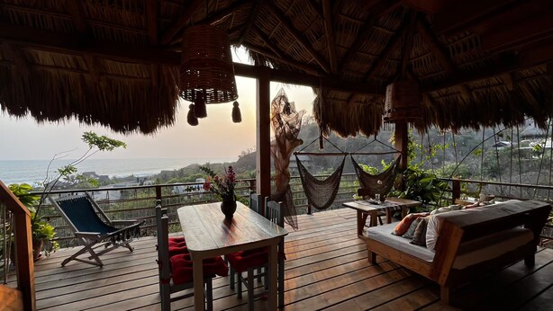 A wooden deck with a table and chairs, a sofa, and two hammocks.
