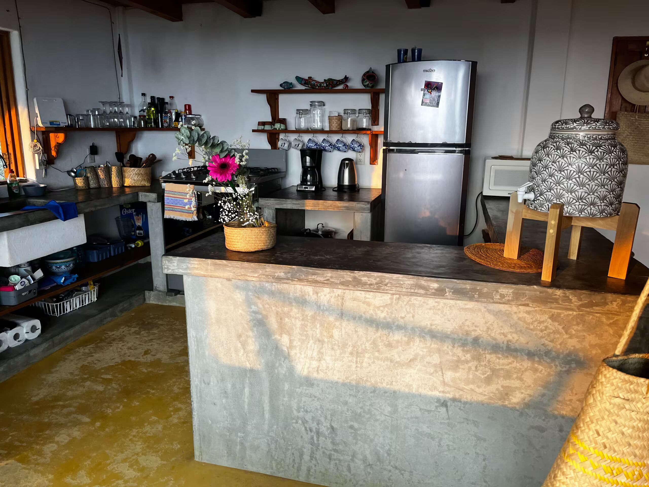Una cocina con una isla central, electrodomésticos de acero inoxidable y distintos utensilios de cocina en estantes.