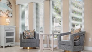 A room with two grey armchairs with floral cushions, a white side table, and a painting on the wall. - North Shore Escape | Heated Pool & Saltwater Canal (North Fort Myers)