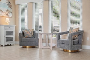 A room with two grey armchairs with floral cushions, a white side table, and a painting on the wall. - North Shore Escape | Heated Pool & Saltwater Canal (North Fort Myers)