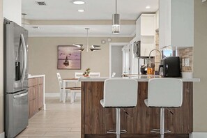 Cozinha moderna com ilha central, banquetas e área de refeições com cadeiras.