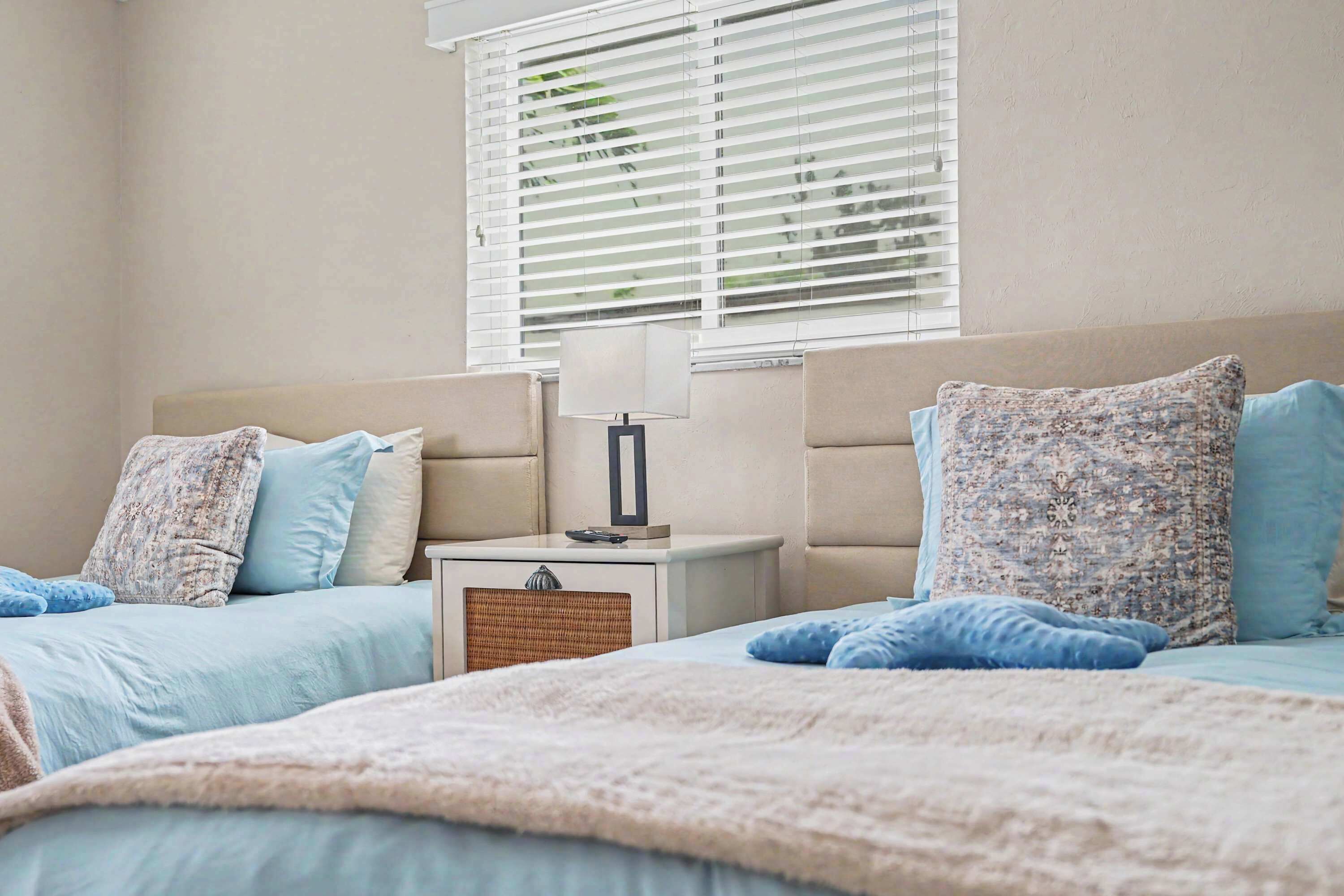 A bedroom with two beds, a nightstand, a lamp, and a window with blinds.