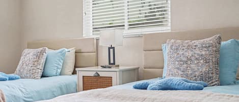 A bedroom with two beds, a nightstand, a lamp, and a window with blinds.