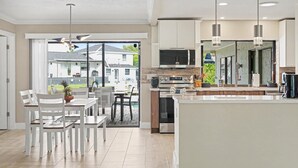 A modern kitchen with a large island, built-in appliances, and a dining area with white furniture. - North Shore Escape | Heated Pool & Saltwater Canal (North Fort Myers)