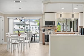 A modern kitchen with a large island, built-in appliances, and a dining area with white furniture. - North Shore Escape | Heated Pool & Saltwater Canal (North Fort Myers)