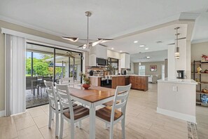 Una cocina moderna con una isla central, comedor con sillas blancas y un amplio ventanal corredera que da a un patio exterior.