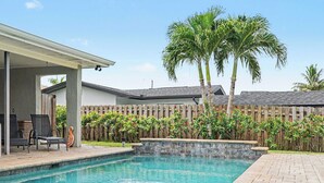 A backyard with a swimming pool, a covered patio area, and a wooden fence. - North Shore Escape | Heated Pool & Saltwater Canal (North Fort Myers)