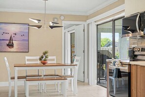 A modern kitchen with a built-in microwave and oven, a dining area with a table and chairs, and a painting of a sailboat on the wall. - North Shore Escape | Heated Pool & Saltwater Canal (North Fort Myers)