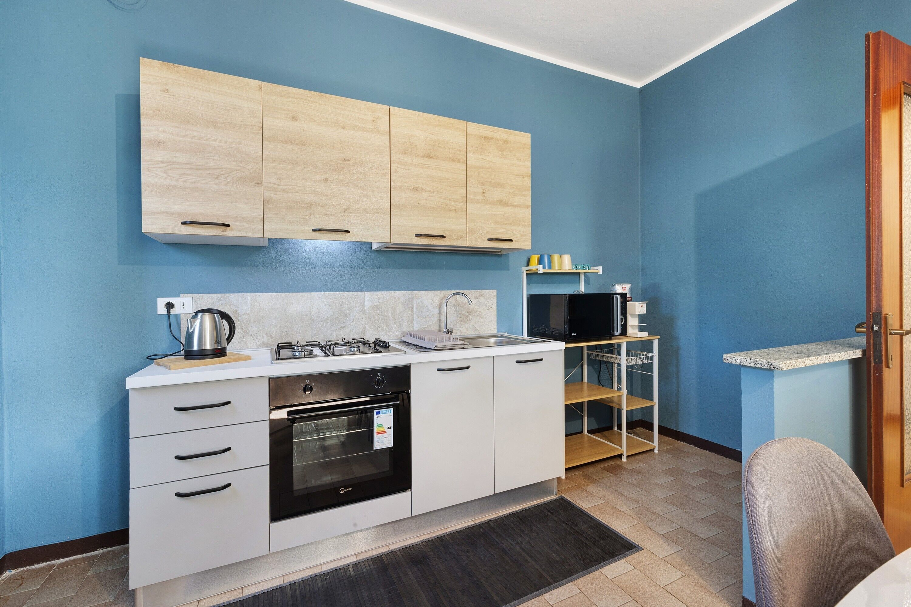 Uma cozinha compacta com armários brancos, forno embutido, fogão a gás e micro-ondas.