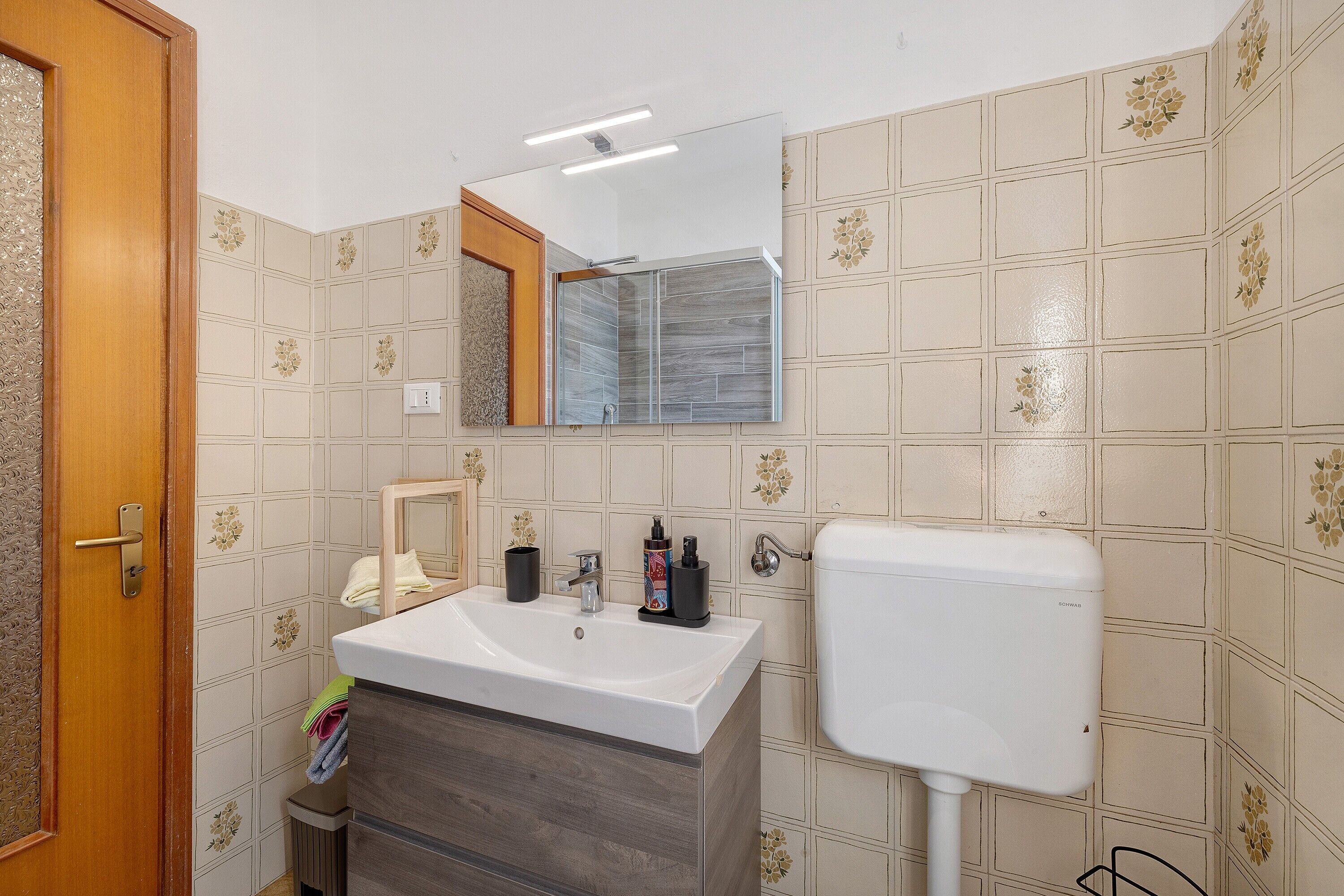 Un baño con lavamanos blanco, espejo, inodoro y basurero.