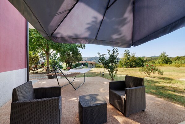 An outdoor patio with wicker furniture, a hammock, and a view of a rural landscape.