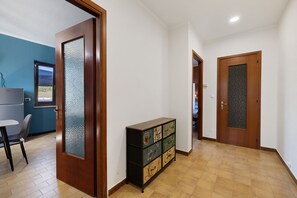 A hallway with a wooden door, a cabinet with multiple drawers, a chair, and a table.