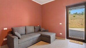 Una habitación con un sofá seccional gris, un ventanal corredero que da a un espacio exterior y suelo de baldosas.