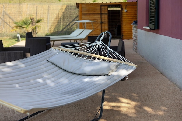 A hammock with a cushion, a table, and chairs in a patio area.