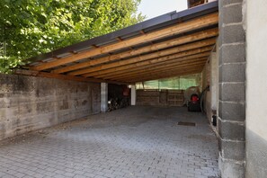 A covered outdoor area with a brick floor, wooden beams, and a brick wall.