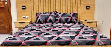 A bed with a geometric patterned bedspread, wooden headboard, bedside tables, and a marble-tiled floor.
