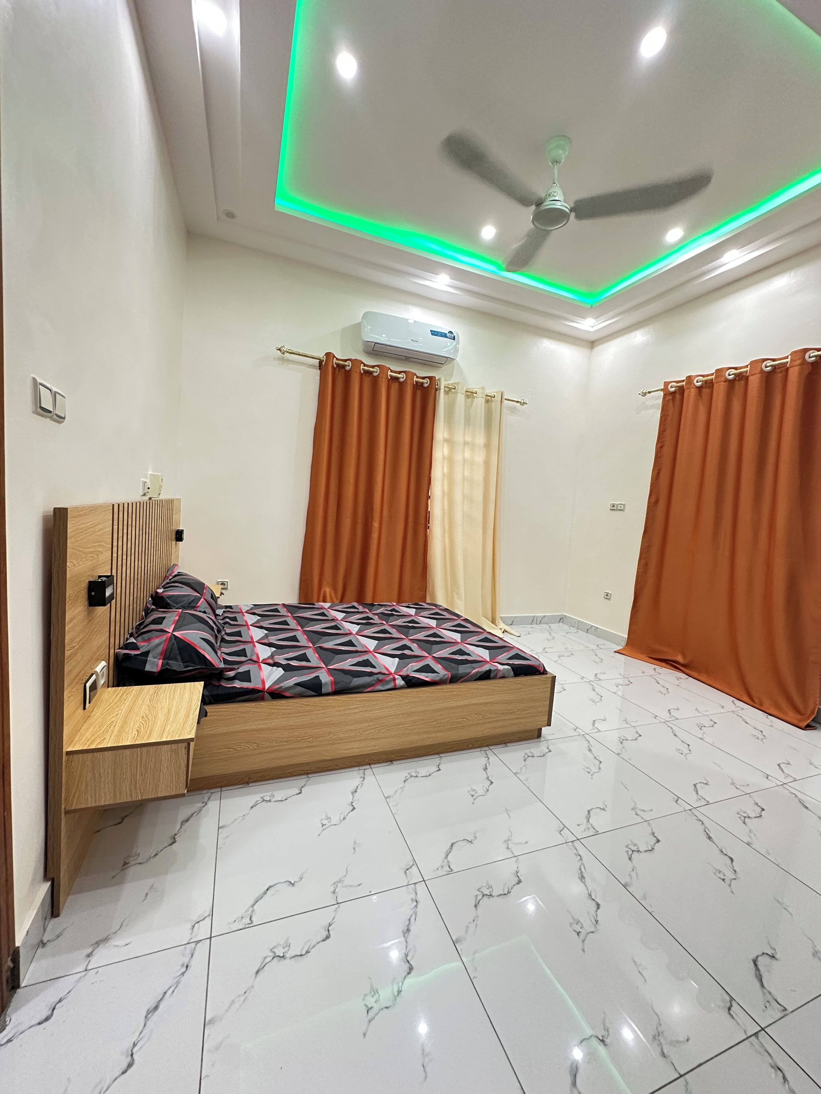 A bedroom with a bed, a ceiling fan, an air conditioning unit, and curtains.