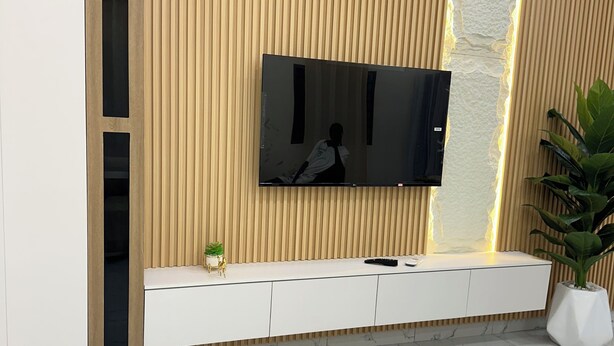 A modern living room with a flat-screen TV mounted on a wooden wall, a white console table, and a marble-tiled floor. - A chic and cozy apartment in the heart of Cotonou (Cotonou)