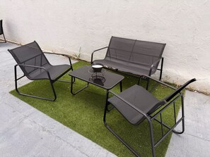 Un ensemble de mobilier d’extérieur comprenant une table et deux chaises, disposé sur une pelouse artificielle devant un mur blanc.