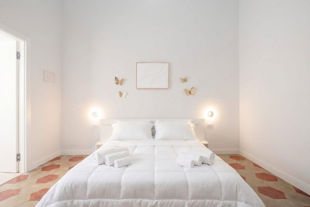 Ein Hotelzimmer mit einem Bett, weißer Bettwäsche, einem gerahmten Bild an der Wand und einer Tür links.